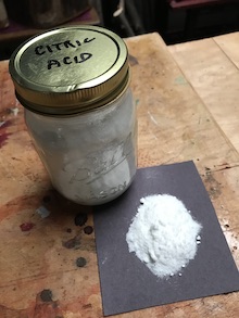 Citric acid crystals in a mason jar w some crystals on a paper square