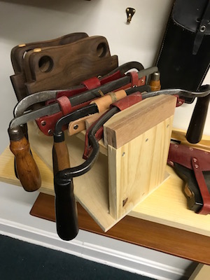 Detail of drawknives and stair saws on a shop made wooden rack from the toolbox.