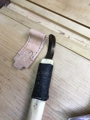The hook knife beside the sewn leather sheath.