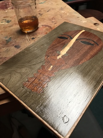 Marquetry face project on wood bench with a jar of shellac.