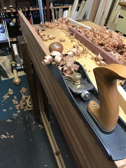 Bench plane atop edge of mahogany board for jointing.