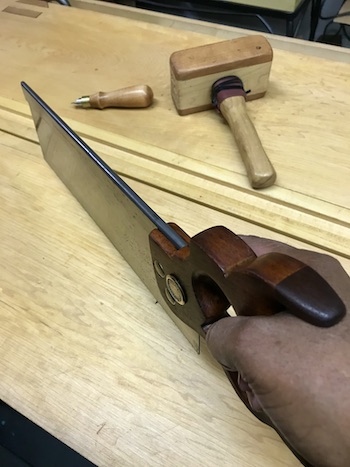Restored saw in hand on wood bench with wood mallet and saw screwdriver.