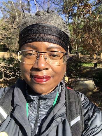 Shirley J in the garden in front of trees.