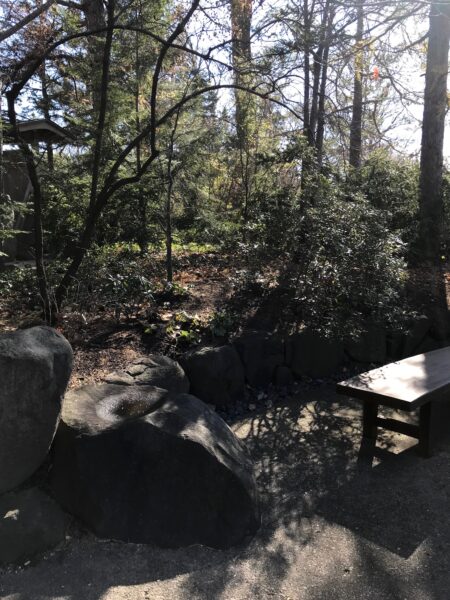 A out the way resting place with a rock and a bench at the garden.