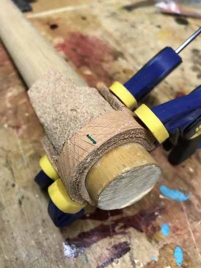 Leather wrapped around a large wood dowel in preparation for wet-forming the sheath.