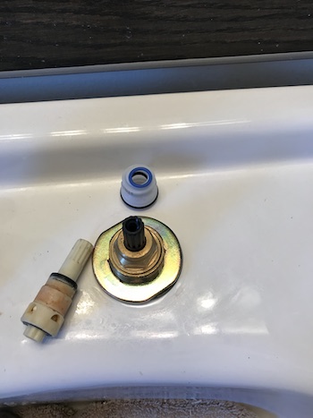 Old cartridge and unused parts beside the newly installed faucet cartridge.