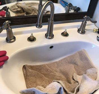 Towels covering the porcelain sink from possible damage during faucet repair.