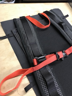Shoulder strap, orange sternum strap and hanging loop attached to back panel of backpack.