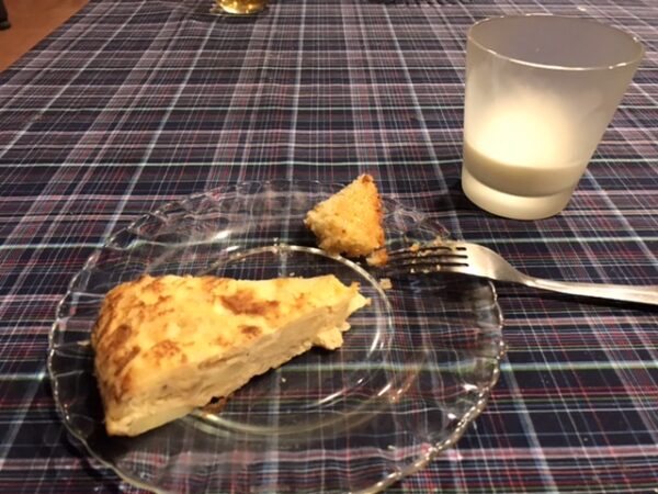 A slice of Spanish tortilla on a breakfast plate with milk.
