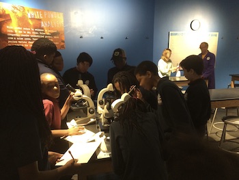 School age children gather around a table to learn scientific research techniques.