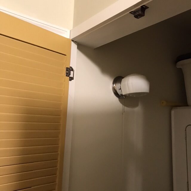 The linen closet door opened showing a wall light and latch.