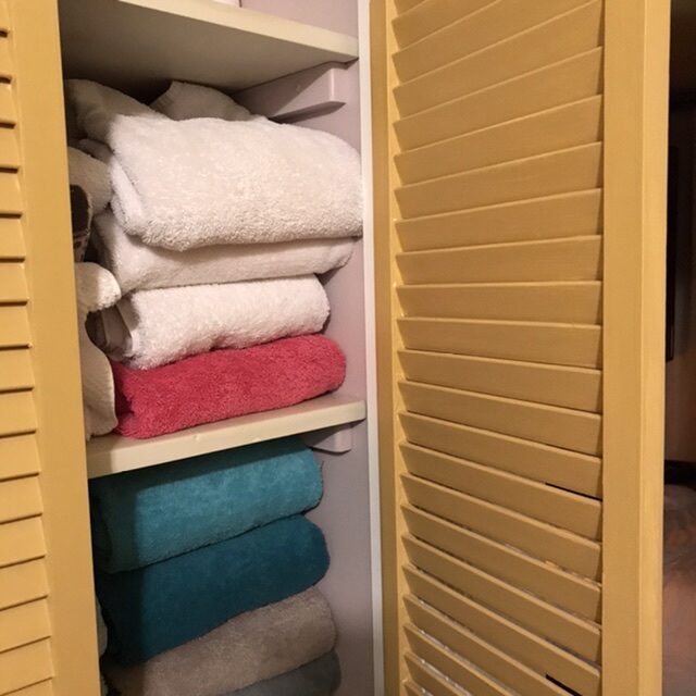 An opened louvered door with towels on the shelf.